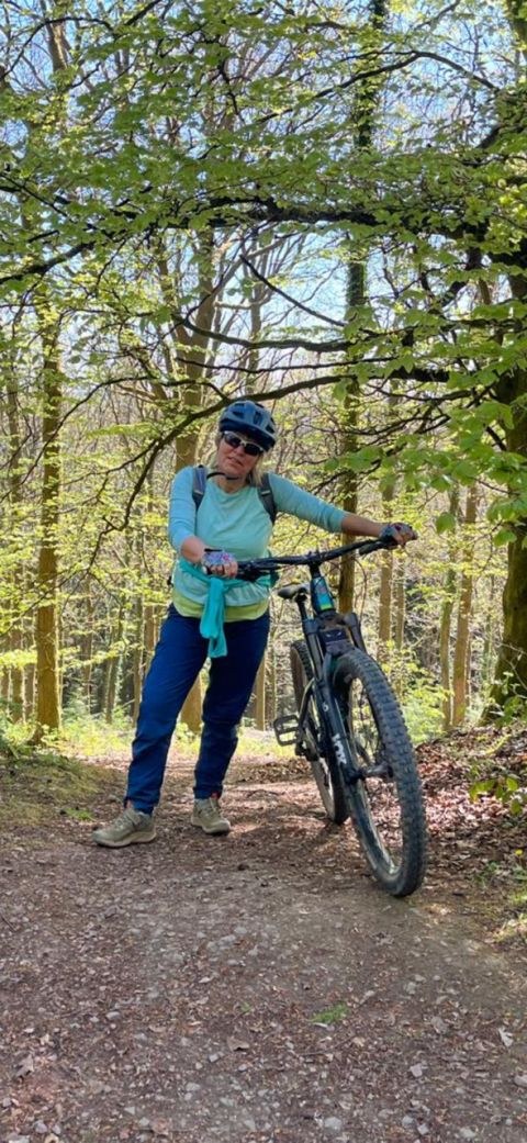 Sarah Taylor Phillips standing with a mountain bike on a woodland trail in spring.