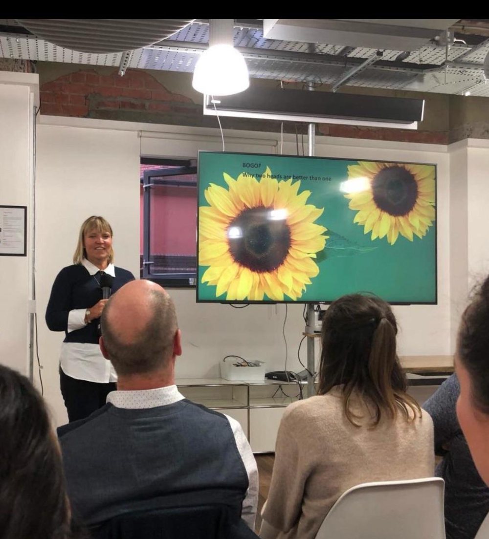 Sarah presenting to a seated audience in a workshop room.
